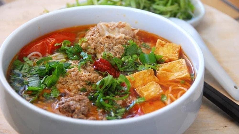 Red tomato-based noodle soup with crab cakes and fresh water spinach